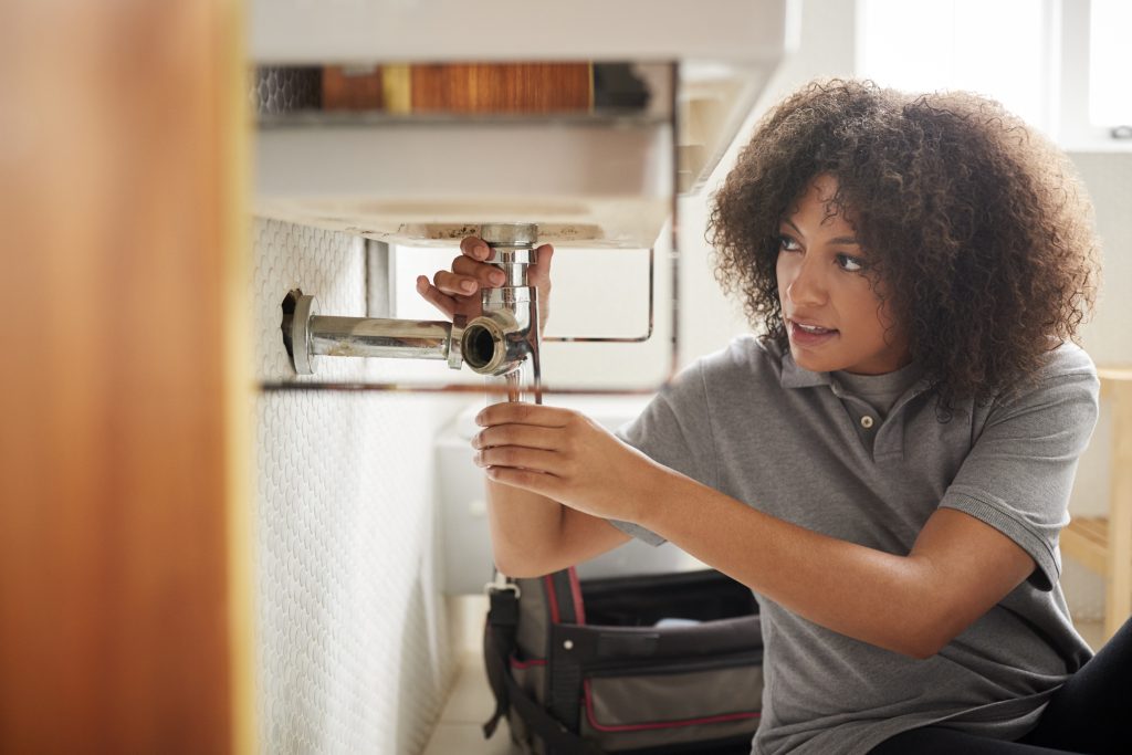 A woman inspecting pipes under a sink for leaks.