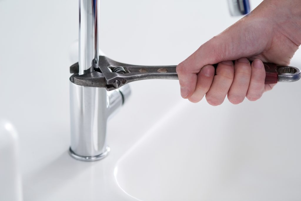 A hand tightening a faucet with a wrench, illustrating a DIY plumbing repair