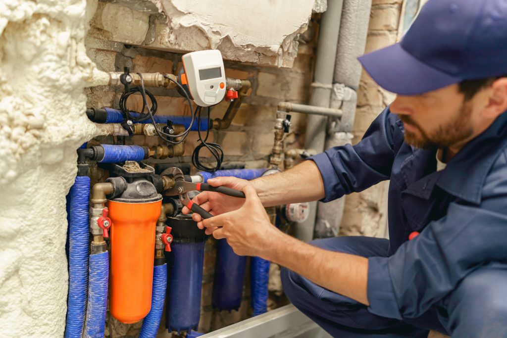 An expert plumber repairing a leaking pipe behind a commercial building wall